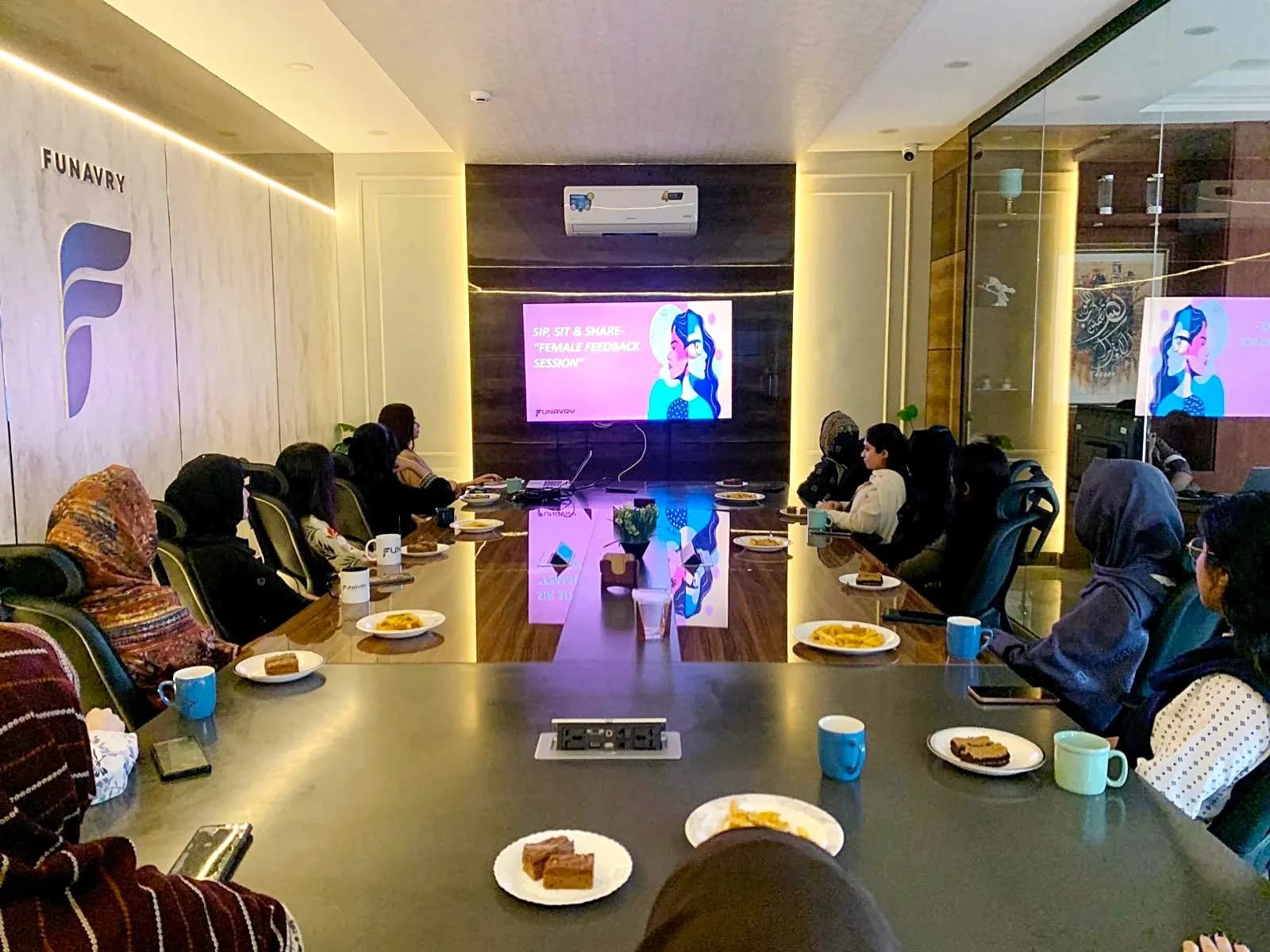 Women of the team seated around the boardroom table for a Sip, Sit & Share feedback session