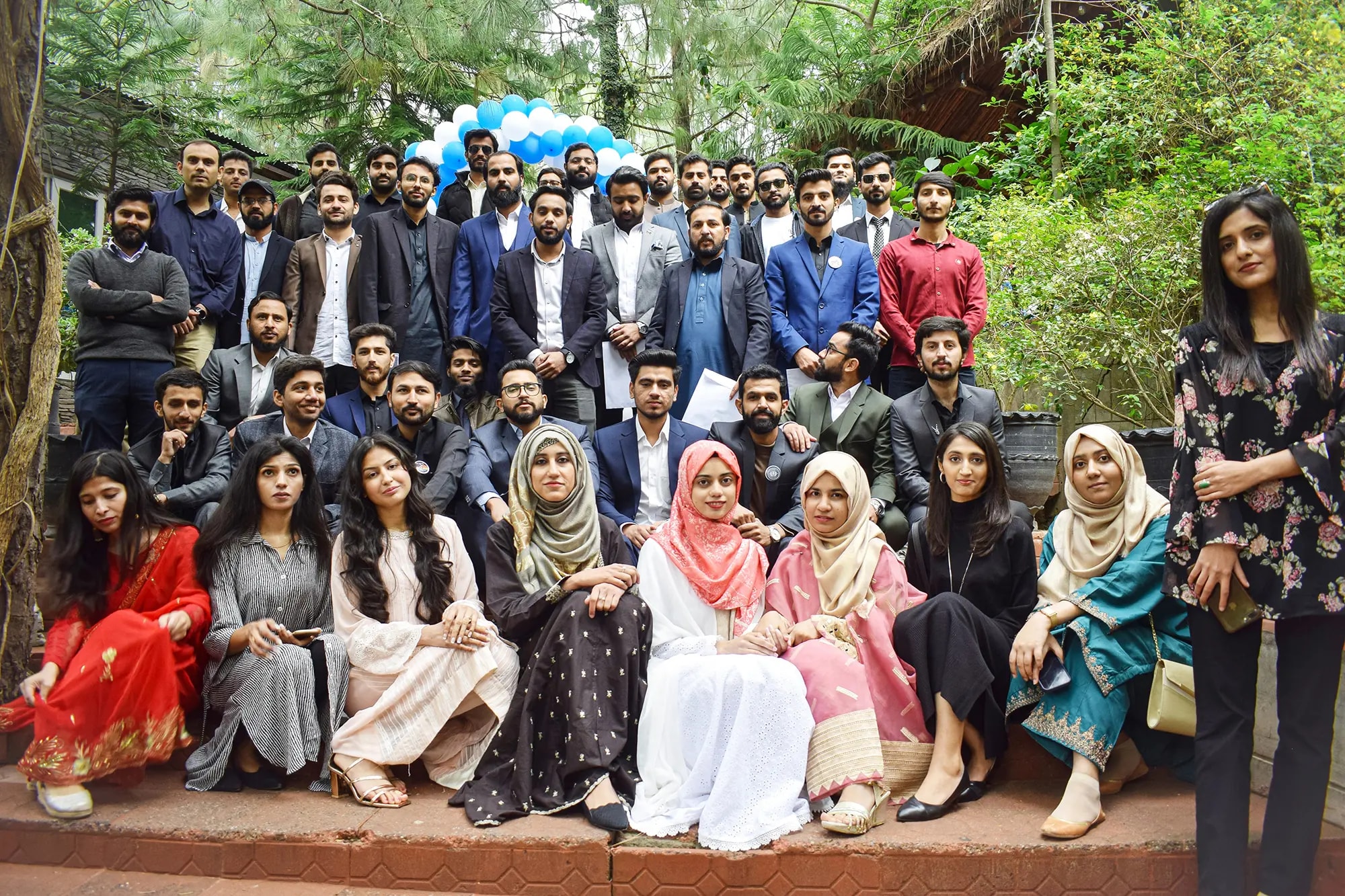 The team dressed formally, gathered among trees under blue and white balloons