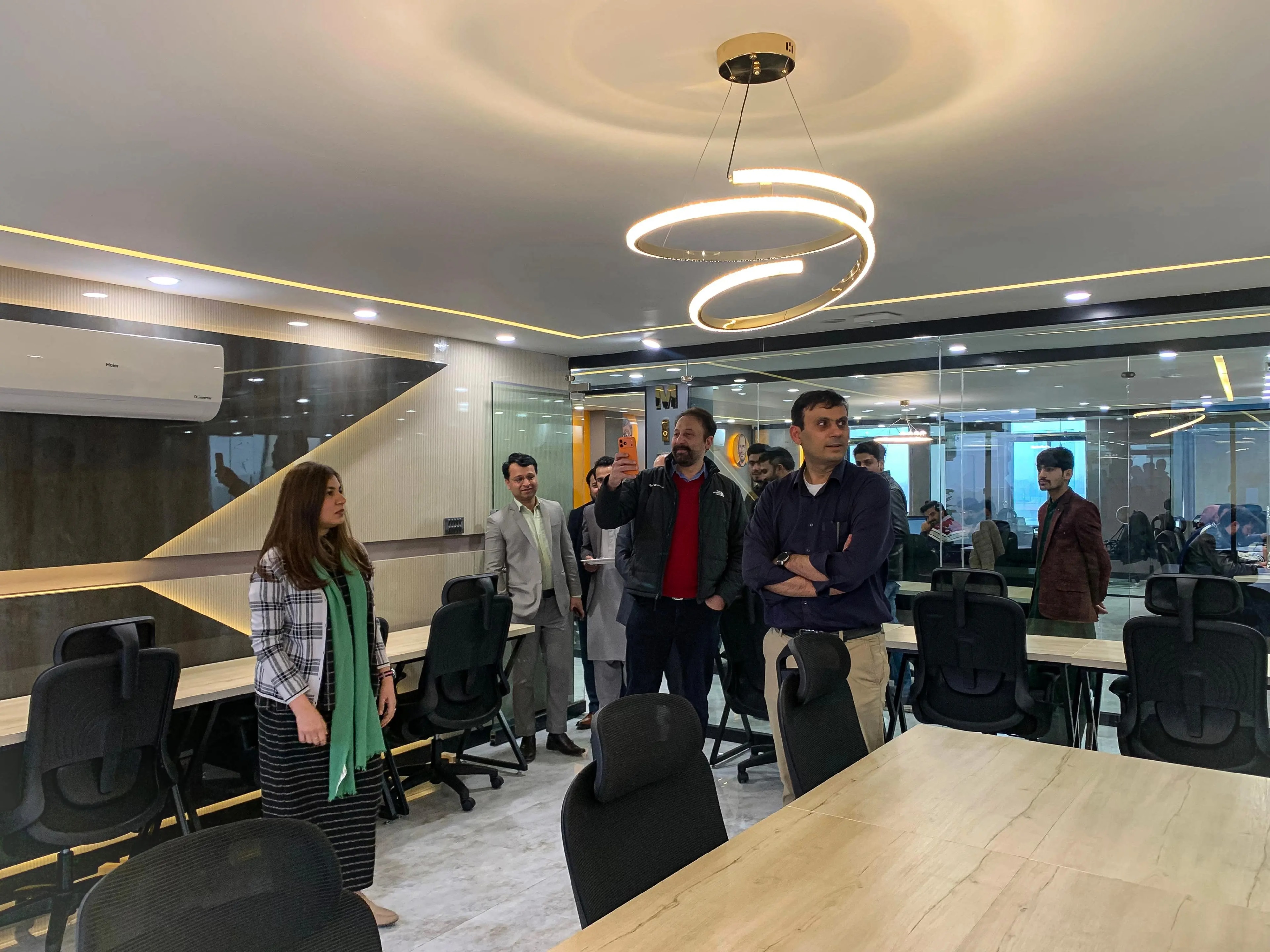 Guests being shown around a meeting room at the office, beneath a spiral pendant light